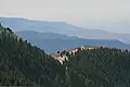 Many mountain ridges recede in the background, growing dinner due to atmosphere. The foreground ridge is covered in evergreens.