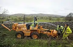 Workers install cables in a trench in a field.