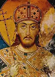 Upper torso and head of a middle-aged bearded man. He wears a domed golden crown, gold-decorated dress and carries a sceptre in the form of a patriarchal cross.